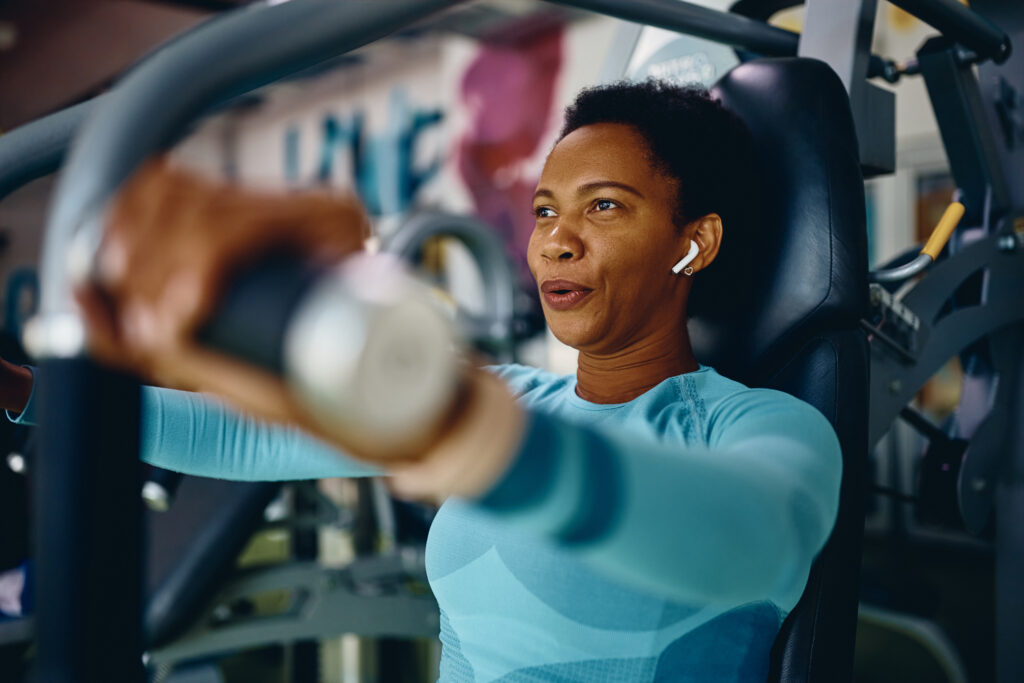 A woman uses a weight machine at the gym for menopause weight gain prevention. 