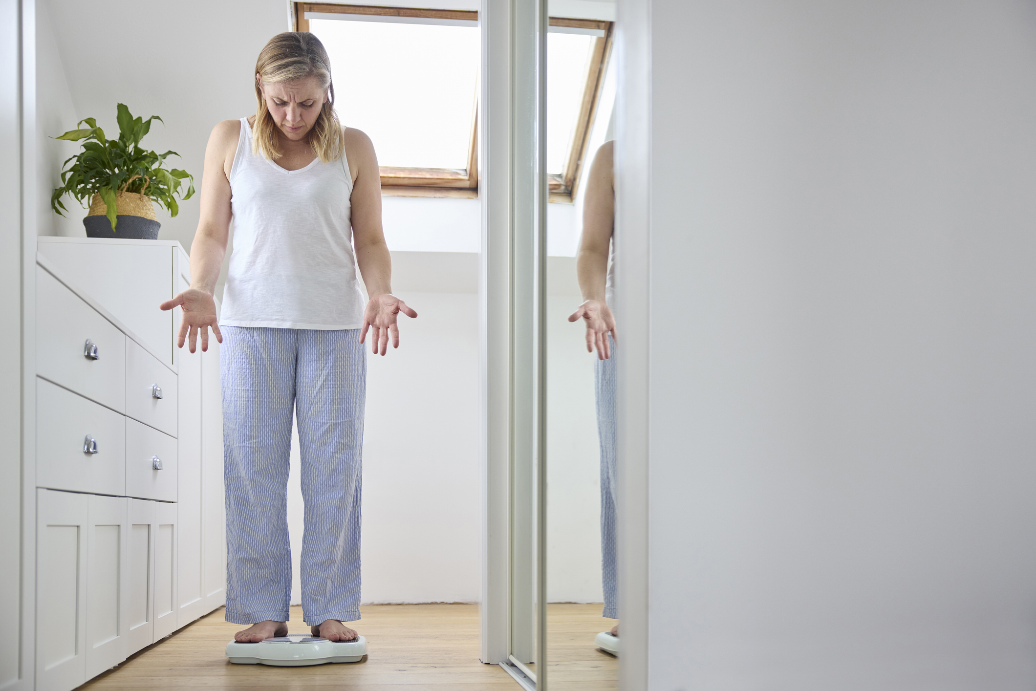 A woman concerned with menopause weight gain stands on a scale in bedroom.