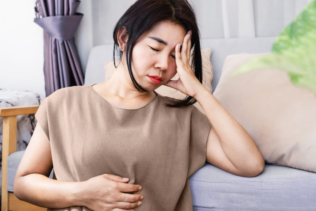 A woman is sitting on the floor in discomfort, holding her stomach and head. 