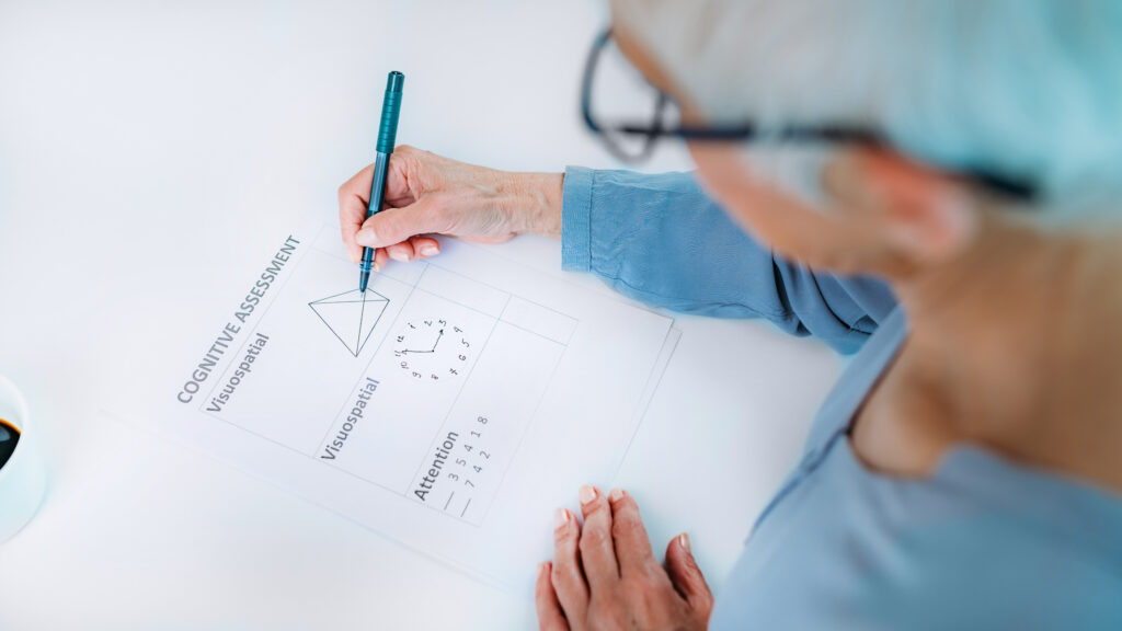 An elderly woman is writing a cognitive assessment. 