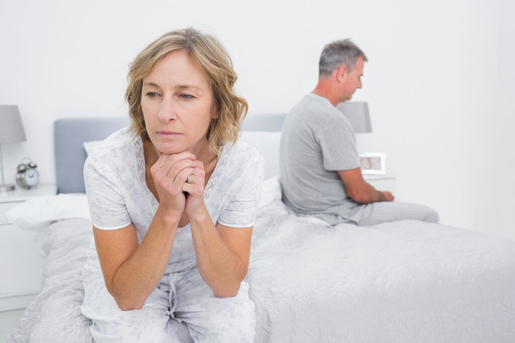 An older women turns away from her husband in the bedroom. 