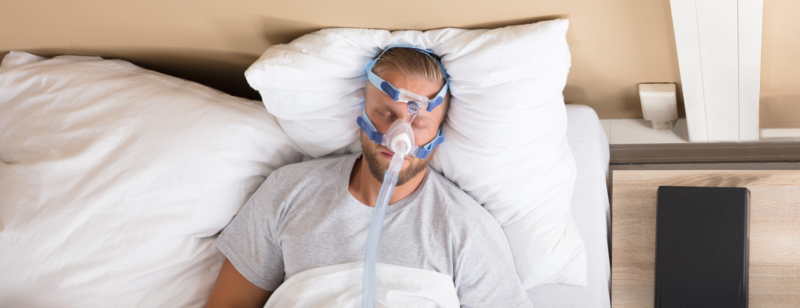 A man lays in bed wearing his CPAP machine. 