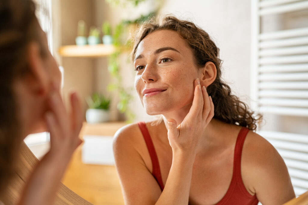 A young woman admires the health of her skin in the mirror. 
