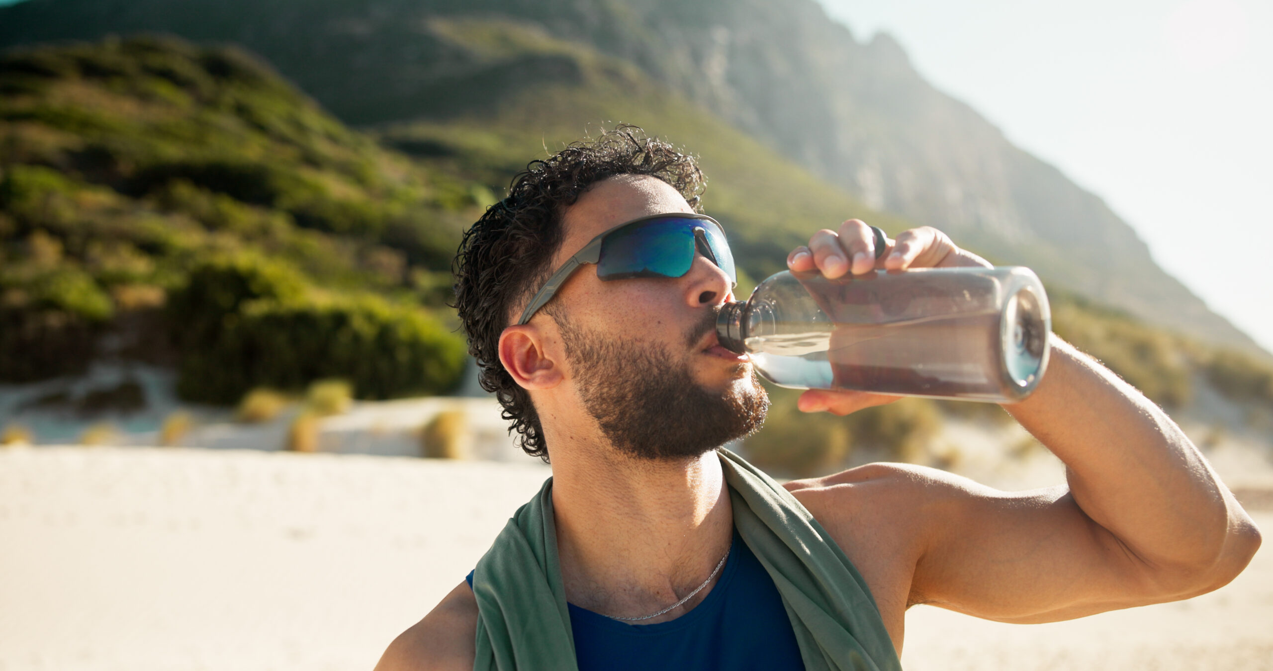 A sweaty man drink water on the beach after a workout.