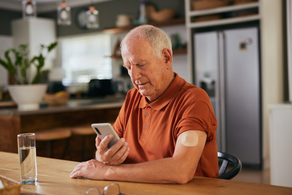 A senior male monitors checks consults his glucose levels on his phone.