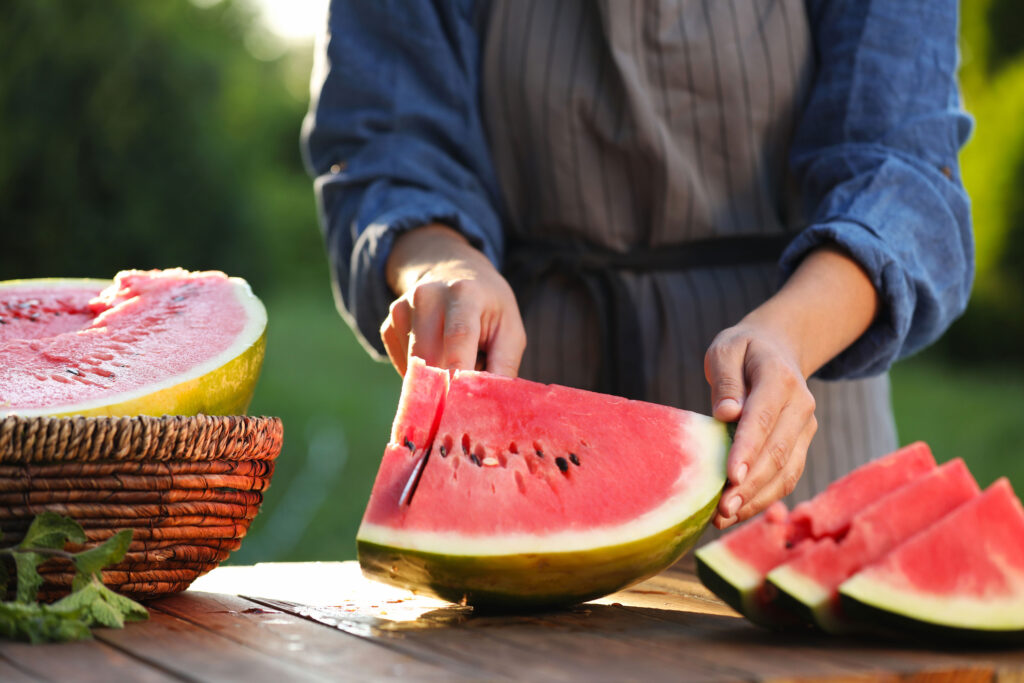 A person is slicing a watermelon outside.