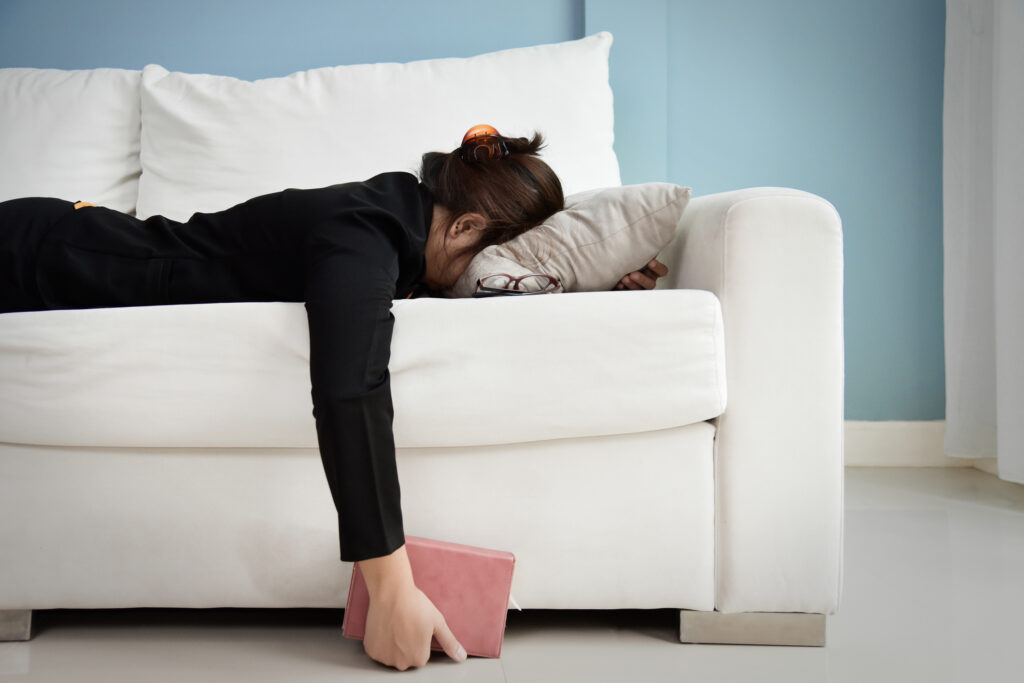 Une femme a l'air fatiguée, allongée à plat ventre sur le canapé. 