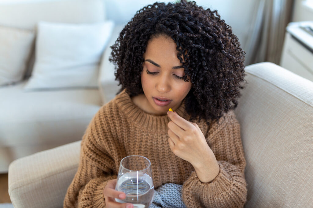 A young woman in her living room takes her medication with a glass of water.