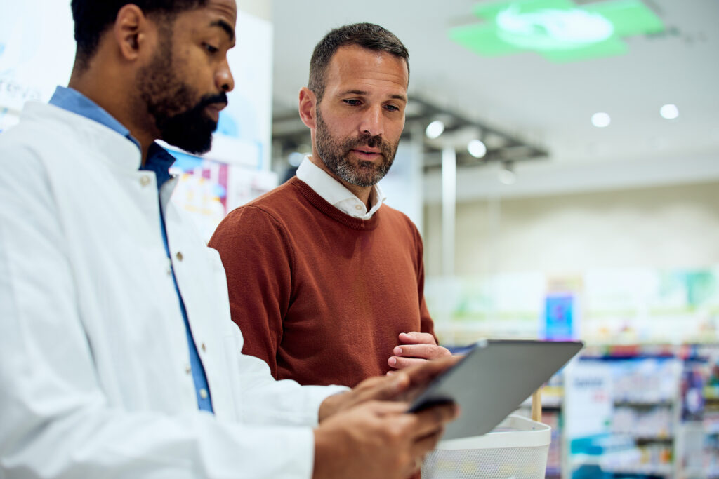 Un homme d'âge mûr consulte ses résultats sur une tablette en compagnie d'un pharmacien. 