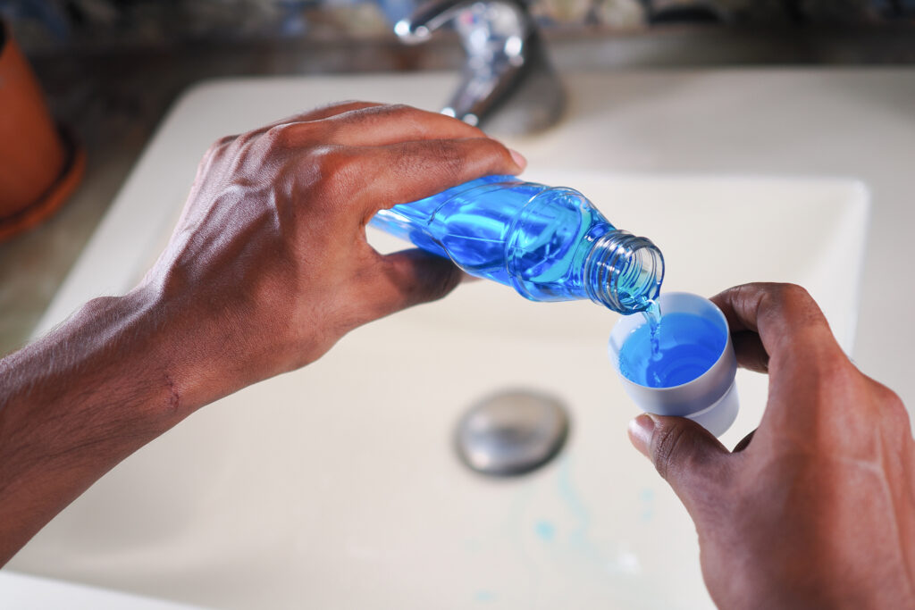 Hands are shown pouring mouthwash into the lid.